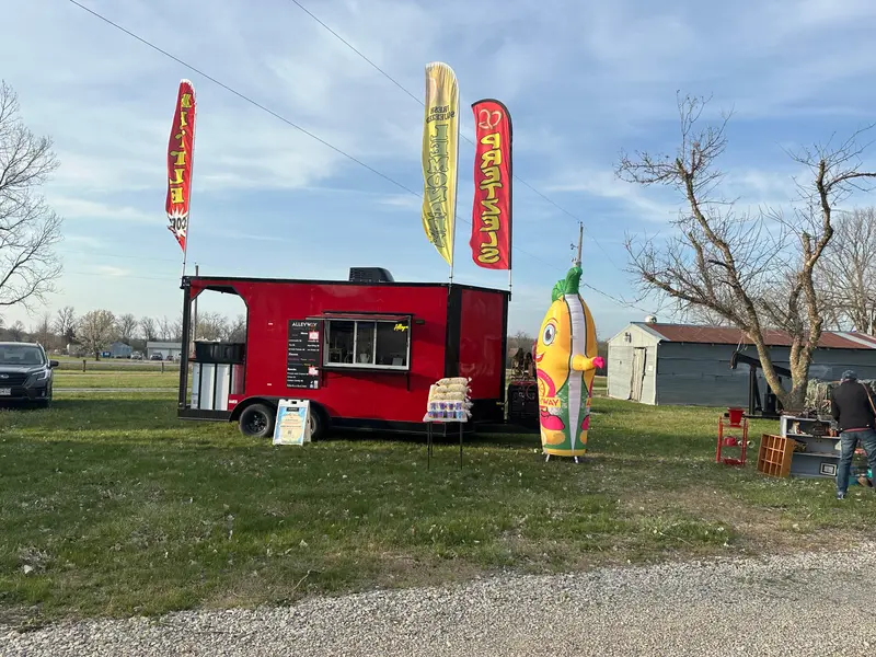 The red Alleyway trailer parked at an outdoor event, feather flags out, at dusk.
